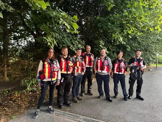 a group of people in vests standing on a sidewalk